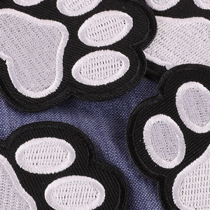 Embroidered animal paw patches in black, grey and white on blue textured fabric