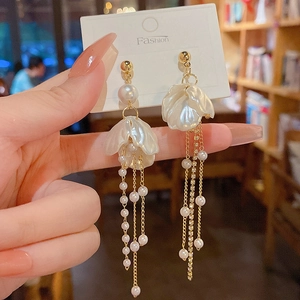Detail of long gold tassel earrings with pearl flower accents and cascading bead chains