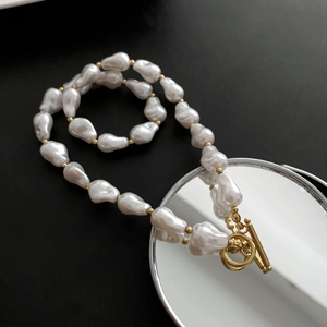 Irregular baroque pearl necklace with gold OT buckle on a sleek black background