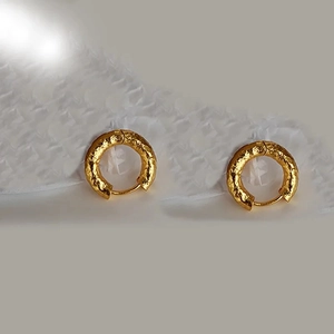 Detail of gold metal hoop earrings with irregular lava texture on white fabric