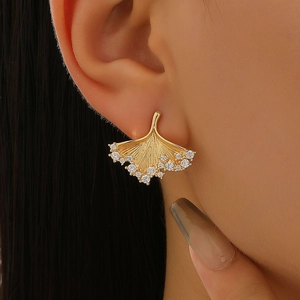 Close-up of golden ginkgo leaf earrings with sparkling cubic zirconia on model