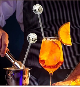Macro shot of silver disco ball cocktail stirrer in a glass with orange slice and ice