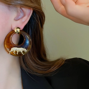 Detail of round tortoiseshell resin earring with golden leopard relief worn by a model
