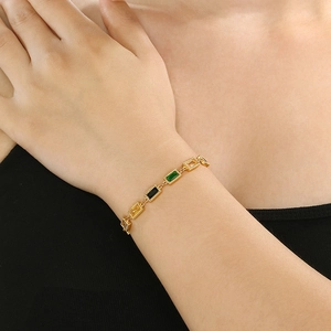 Close-up of a gold stainless steel bracelet with green and black heart charms on a model