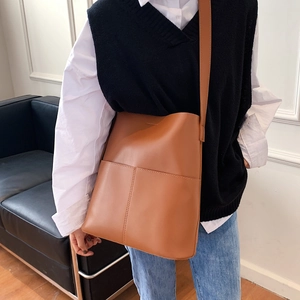 Braune Lederbeuteltasche am Modell mit weißem Hemd und Jeans in Innenraumumgebung