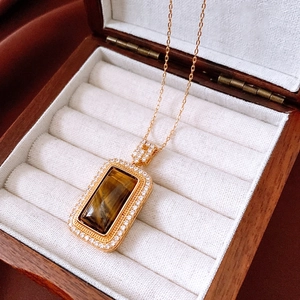 Close-up of a gold-plated tiger eye square pendant with white zircon halo in a wooden box