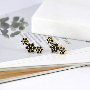 Close-up of flower-shaped gold earrings with black stones on a lifestyle magazine