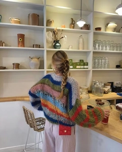 Rear view of a loose-fitting rainbow striped knit sweater in a cozy cafe setting
