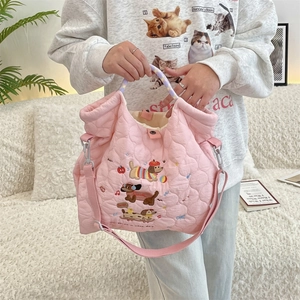 Quilted pink crossbody bag with dog embroidery shown being held in a cozy home setting