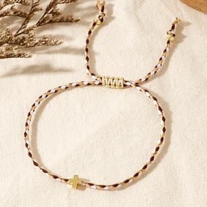 Close-up of handmade woven cross bracelet with golden metallic detail and adjustable cord