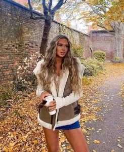 Outdoor street style view of a brown suede vest with white faux fur lining and trim