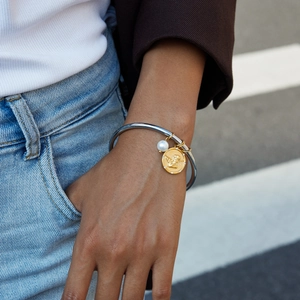 Detail of vintage steel bracelet with pearl and gold angel pendant on a woman's wrist