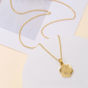 Macro shot of hexagonal gold pendant necklace with engraved letter Q and radiating texture