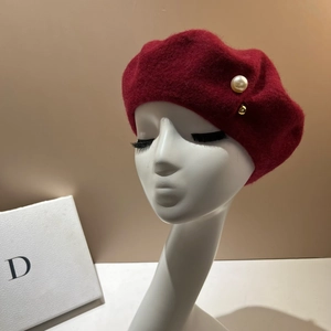 Detailed close-up of dark red wool beret featuring a large pearl and golden metal rivet