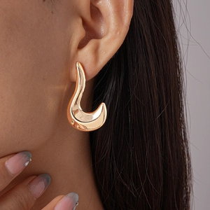 Macro detail of minimalist gold flame-shaped ear studs worn by model on ear