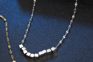 Macro shot of silver beaded chain with cubic pendants on a textured navy background
