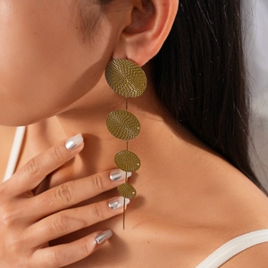Close-up of woman wearing long gold tiered earrings with textured geometric disc patterns