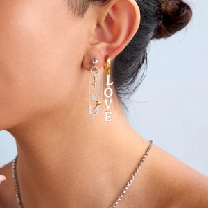 Close-up of asymmetric LOVE letter chain earrings and silver paperclip design on a model