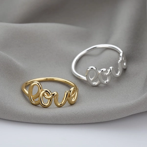 Minimalistische Love-Ringe in Gold und Silber auf dunklem strukturiertem Stoff