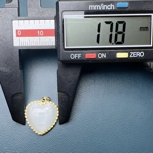 Macro shot showing heart-shaped gold pendant width being measured at 17.8mm with a digital caliper