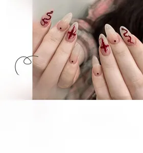 Macro detail of almond press-on nails featuring red snake and cross art on nude gradient