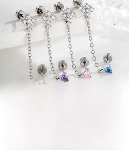 Detail view of steel cartilage piercings with colored heart zircons and chain connection