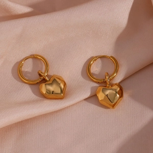 Macro shot of gold-plated geometric heart charm hoop earrings on soft pink satin fabric