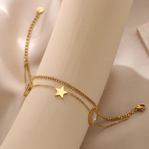 Close-up of golden double-layer titanium bracelet with star charms on a beige stand