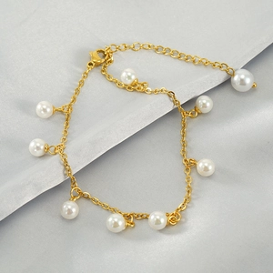 Detail of gold titanium steel anklet with white pearl tassels on grey silk fabric