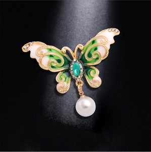 Elegant butterfly brooch with green enamel, crystals and hanging pearl on black background