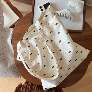 Detailed top view of a cream canvas tote bag with black bow prints on a wooden table