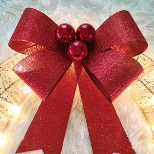 Detail of red glitter bow ornament with red berries on white faux fur and warm LED lights