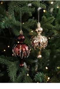 Detail of burgundy and champagne gold teardrop Christmas ornaments hanging on a pine tree