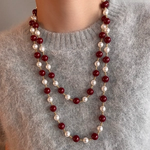 Dettaglio di collana a doppio filo con perle rosse e bianche su maglione grigio lavorato