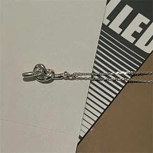 Detailed close-up of a minimalist silver knotted necklace resting on branded stationery