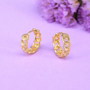 Close-up of golden chain link hoop earrings on a light purple surface with flowers