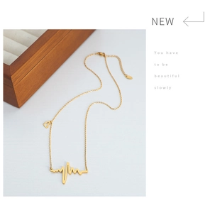 Detail of gold heartbeat pendant necklace with small heart charm on a minimalist chain