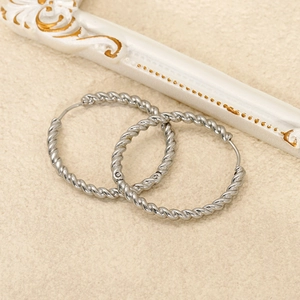 Macro shot of silver twisted rope hoop earrings on a vintage beige background texture