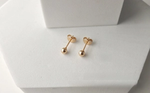 Gros plan de boucles d'oreilles boules dorées sur un présentoir géométrique