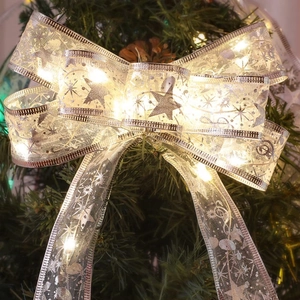 Close-up of golden Christmas ribbon bow with warm LED lights on a pine tree branch