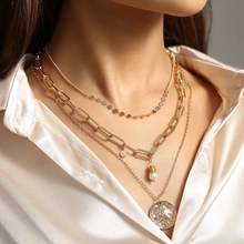 Detailed close-up of layered gold necklace set with pearl and textured disc pendants