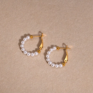 Macro detail of gold C-shaped stainless steel earrings with white pearls on beige fabric