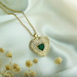 Detail of gold heart necklace with emerald green stone on white silk background