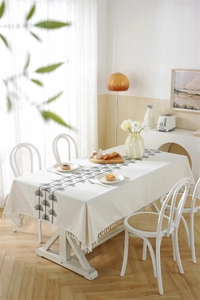 Detailed close-up of beige rectangular tablecloth with black embroidery and tassels