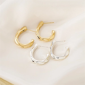 Detail of twisted texture C-shape earrings in gold and silver finishes on white silk