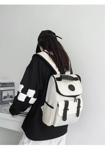 Detail of a black and white canvas backpack featuring a flap closure and front pocket