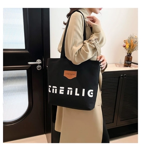Close-up of black canvas tote bag with CNERLIG print and brown leather detail on shoulder