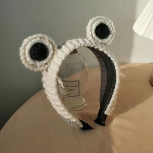 Detailansicht eines weißen Strickstirnbands mit niedlichen Froschaugen auf Glasstütze