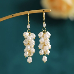Macro detail of elegant golden drop earrings with clustered white teardrop pearls