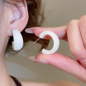 Gros plan de boucles d'oreilles blanches en C en résine mate portées par un mannequin